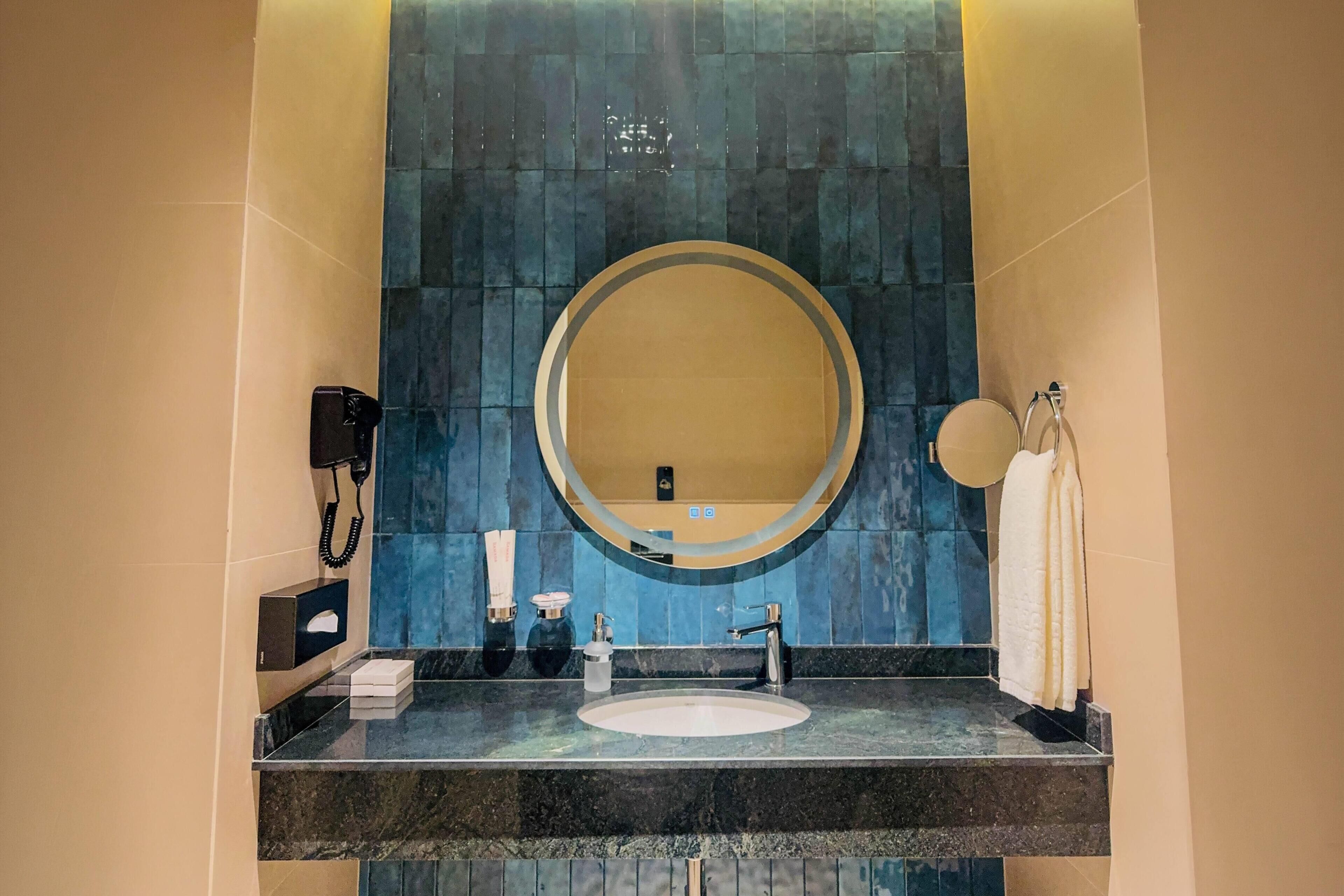 A bathroom with a round mirror, a sink, and a phone on the wall.