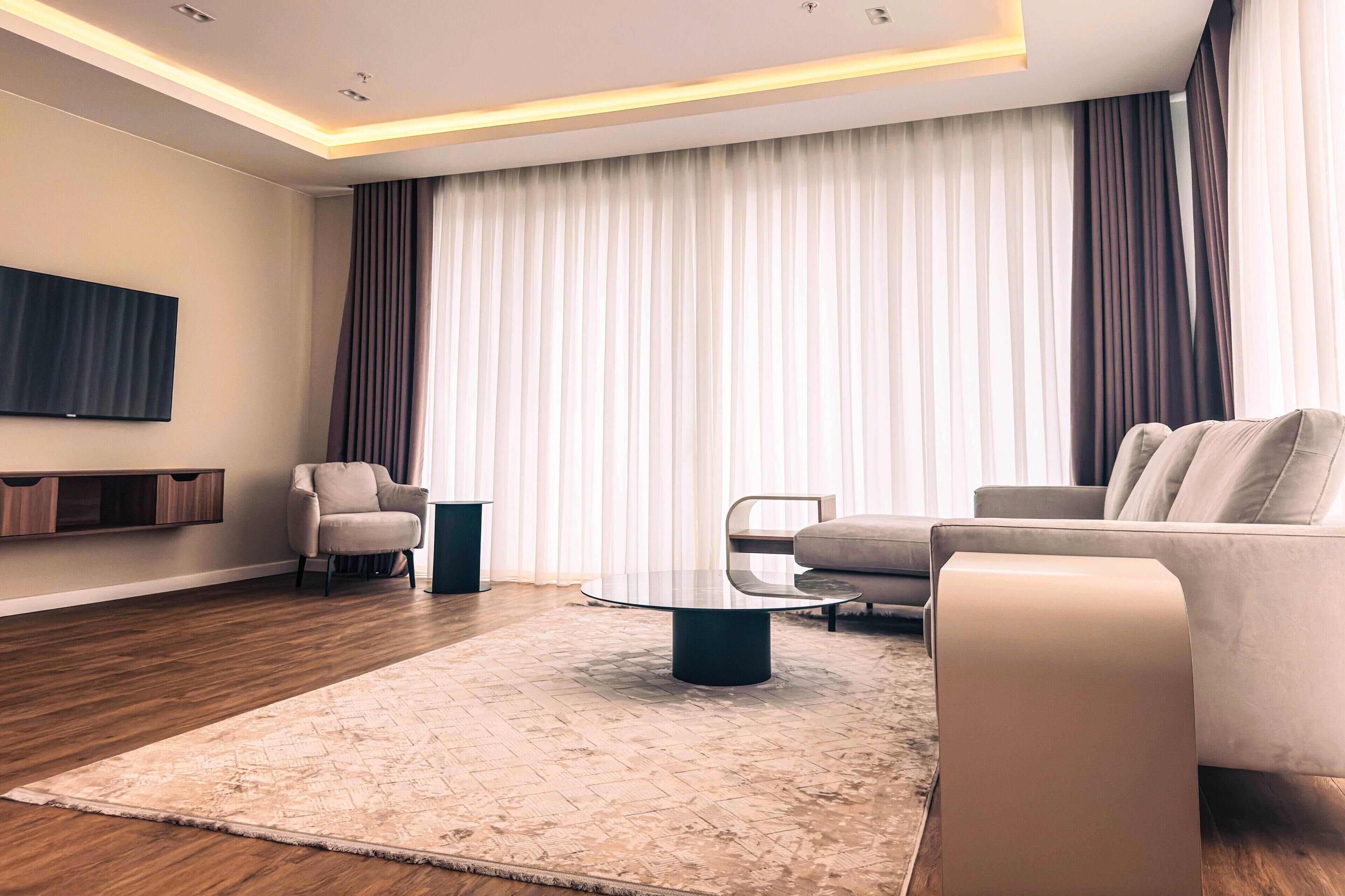 A modern living room with a round glass coffee table, a beige sofa, and a flat-screen TV mounted on the wall.