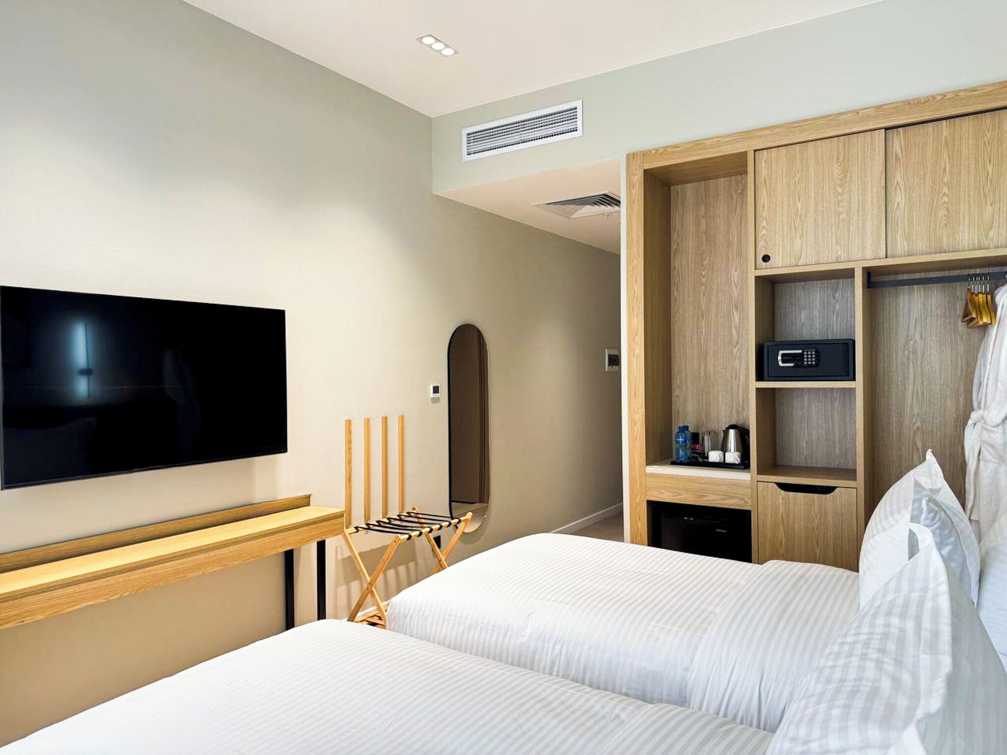A hotel room with a bed, a TV, a wooden wardrobe, and a small shelf with toiletries.