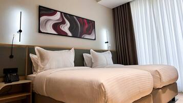 A hotel room with two beds, a painting on the wall, a telephone on the nightstand, and a window with curtains.