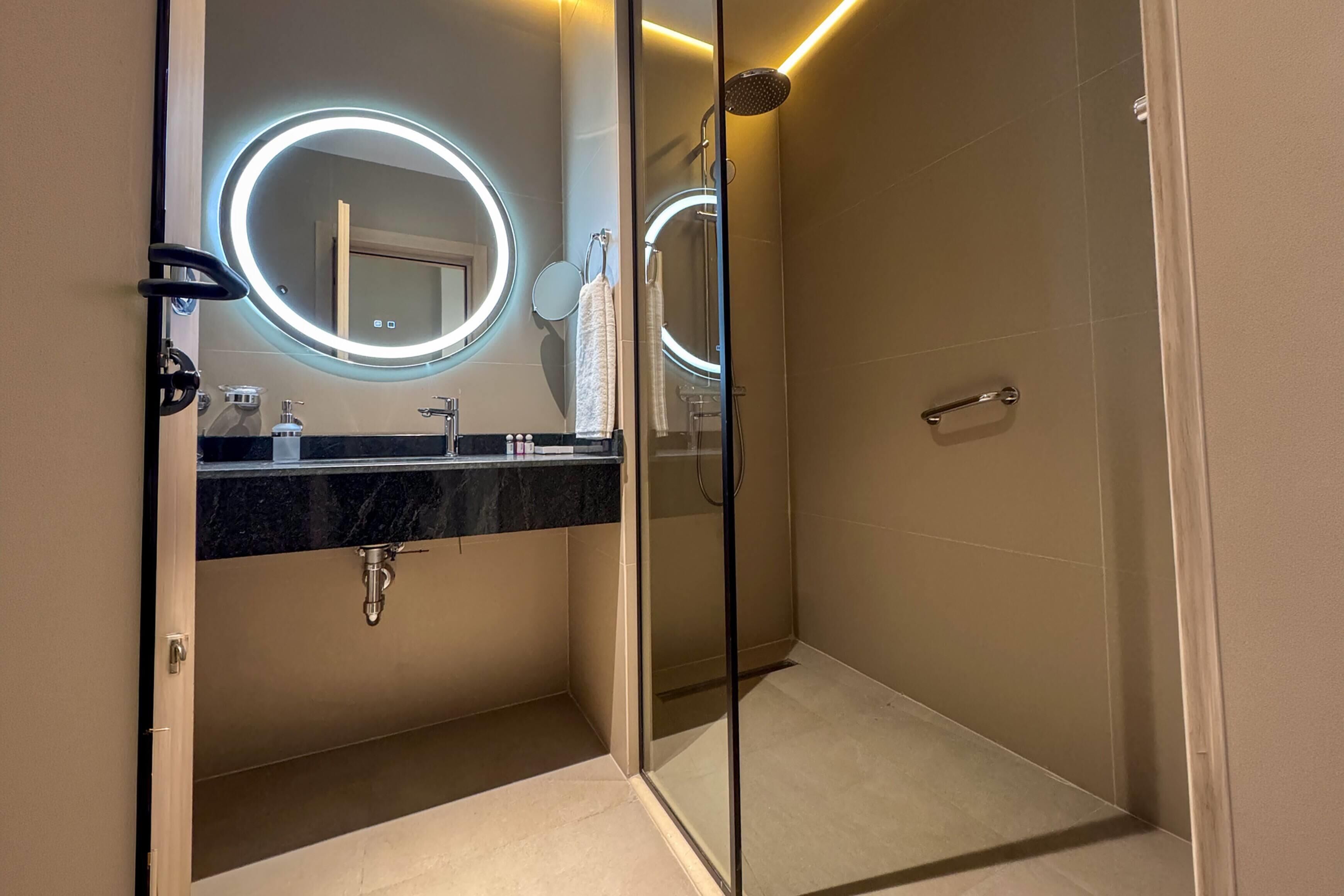 A modern bathroom with a glass shower enclosure, a vanity with a marble countertop, and illuminated mirrors.