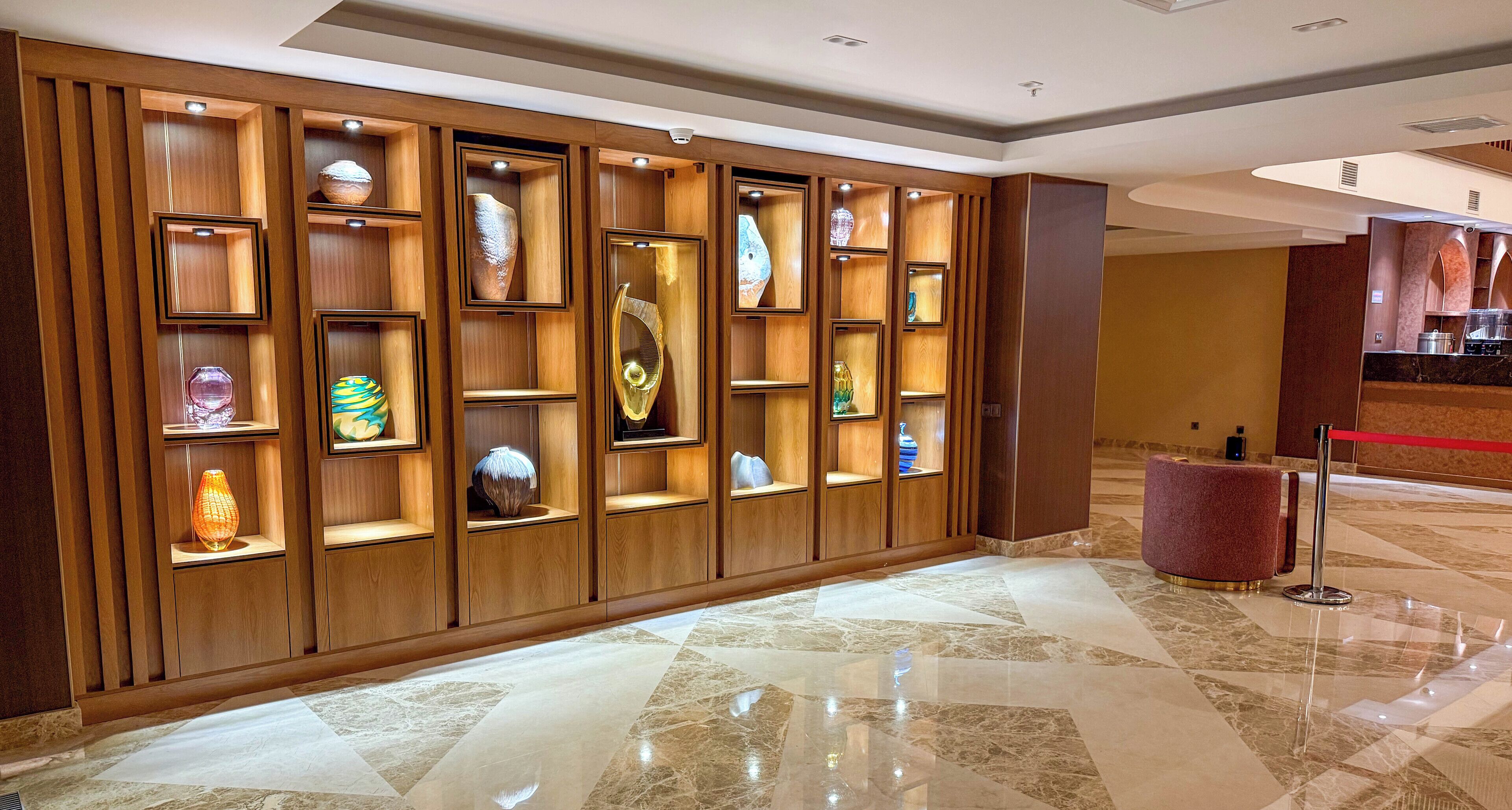 A lobby with a wooden panel wall displaying various decorative items, a marble floor, and a reception area with a red rope barrier.