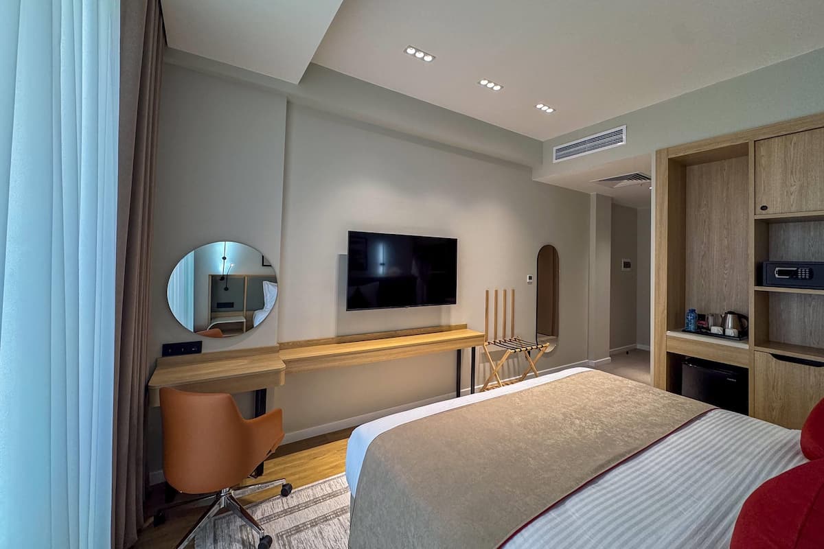 A modern hotel room with a bed, a desk, a chair, a TV, and a wardrobe.