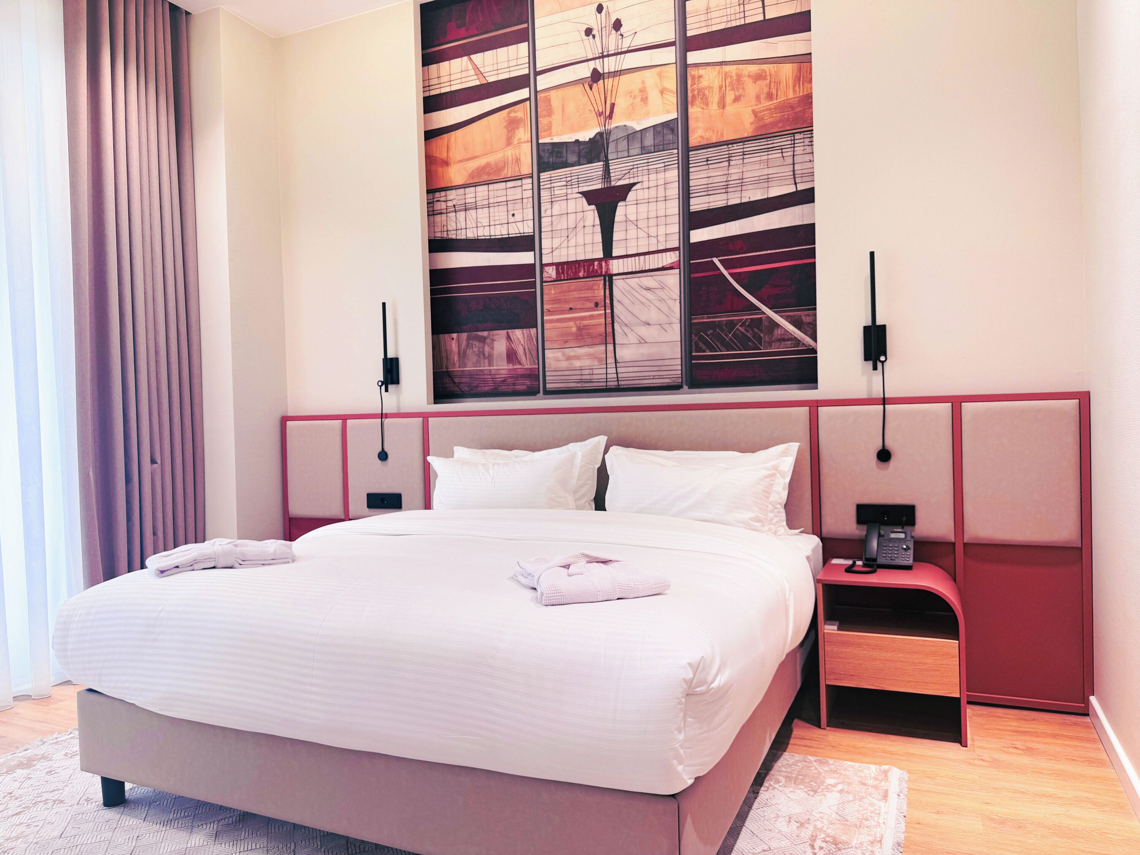 A modern hotel room with a large bed, a nightstand, a telephone, and a wall art piece.