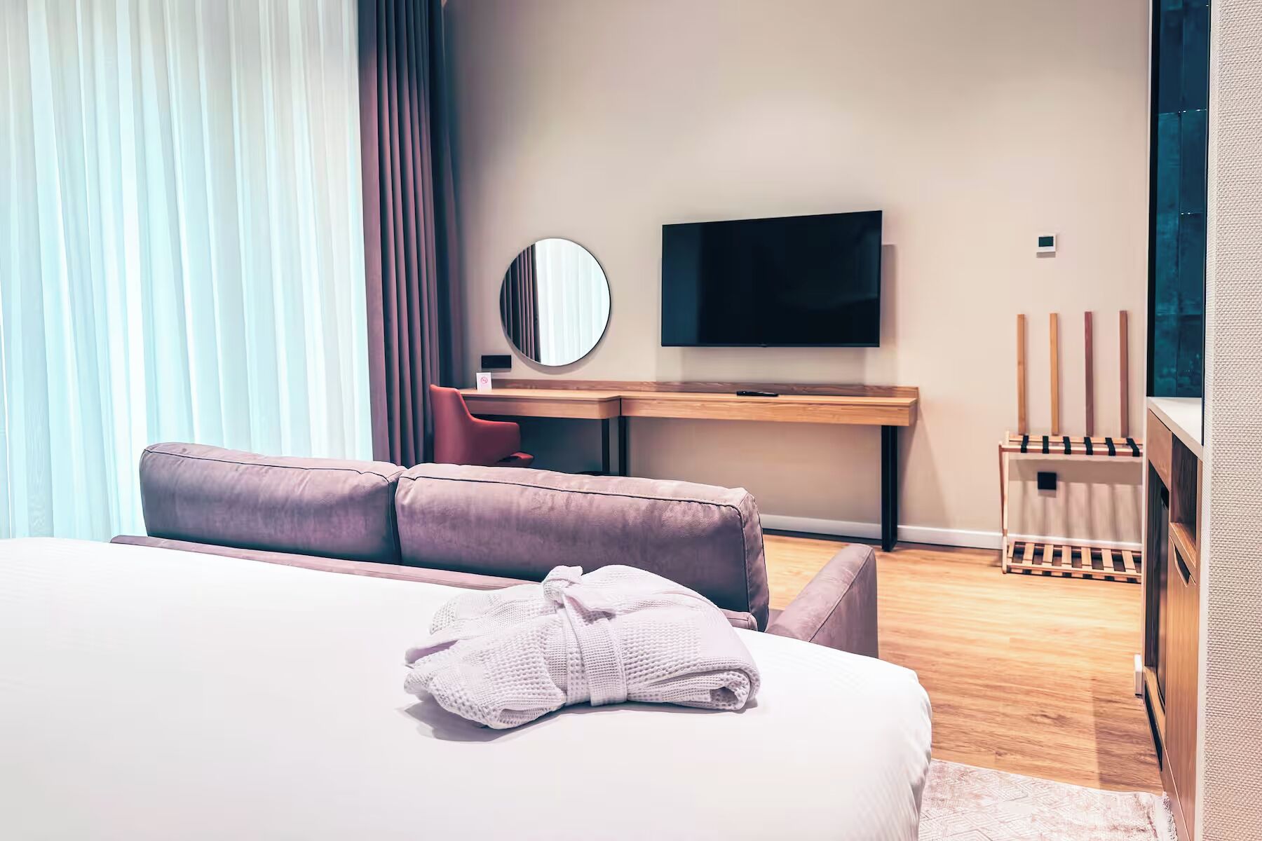 Une chambre d’hôtel moderne équipée d’un lit, d’un bureau, d’une télévision et d’une fenêtre avec des rideaux.