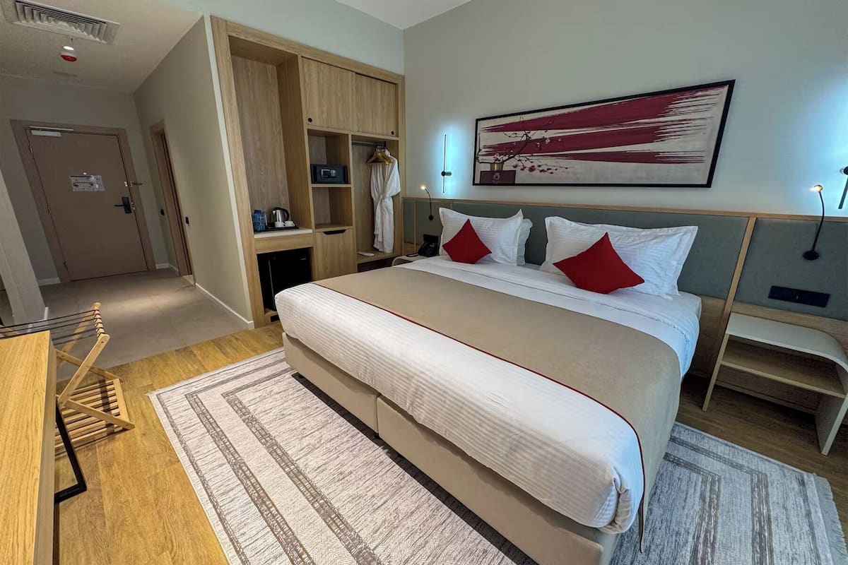 A hotel room with a large bed, a wardrobe, a desk, and a painting on the wall.