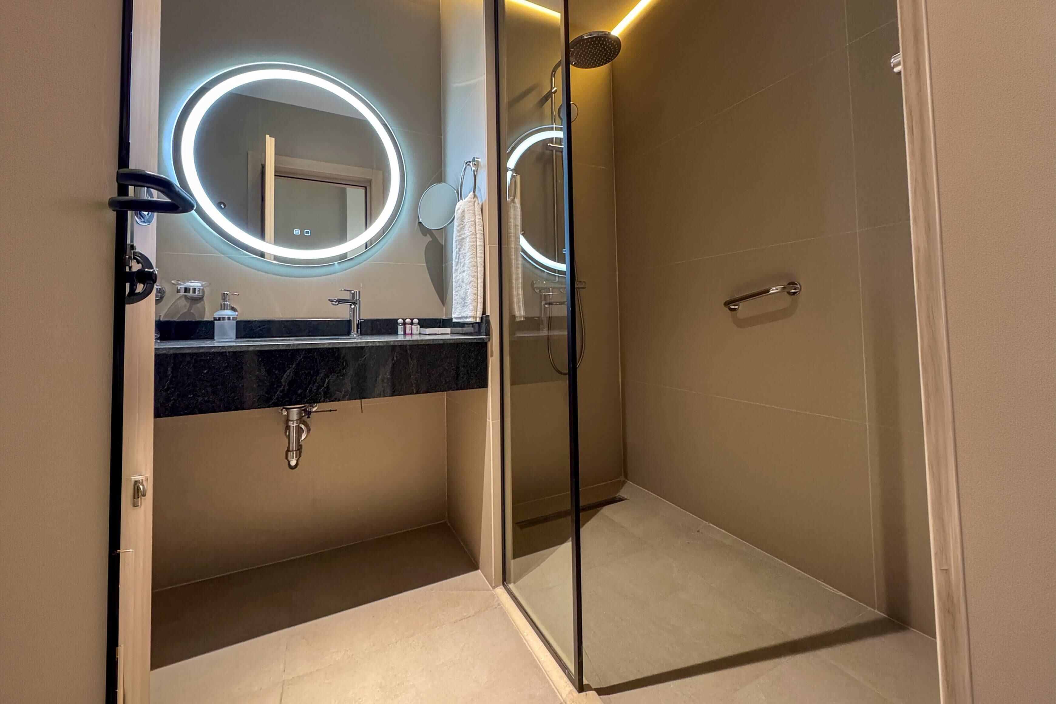 Un baño moderno con ducha envuelta en vidrio, encimera de mármol y espejos iluminados.