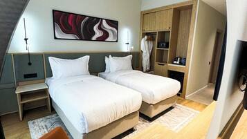 A modern bedroom with two beds, a wooden desk, a wardrobe, and a painting on the wall.