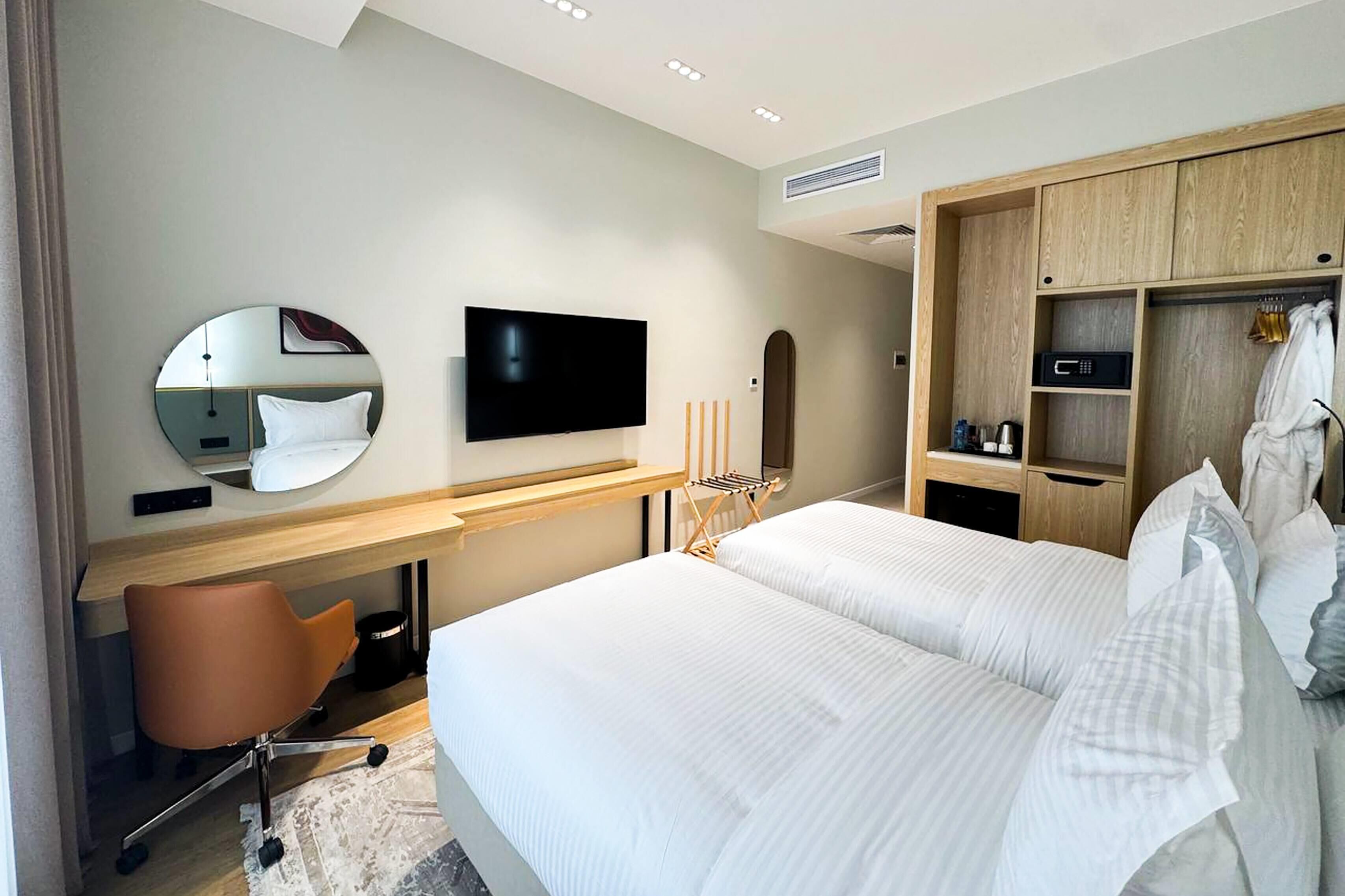 Een moderne hotelkamer met een bed, een bureau met stoel, een televisie, een spiegel en een kledingkast.