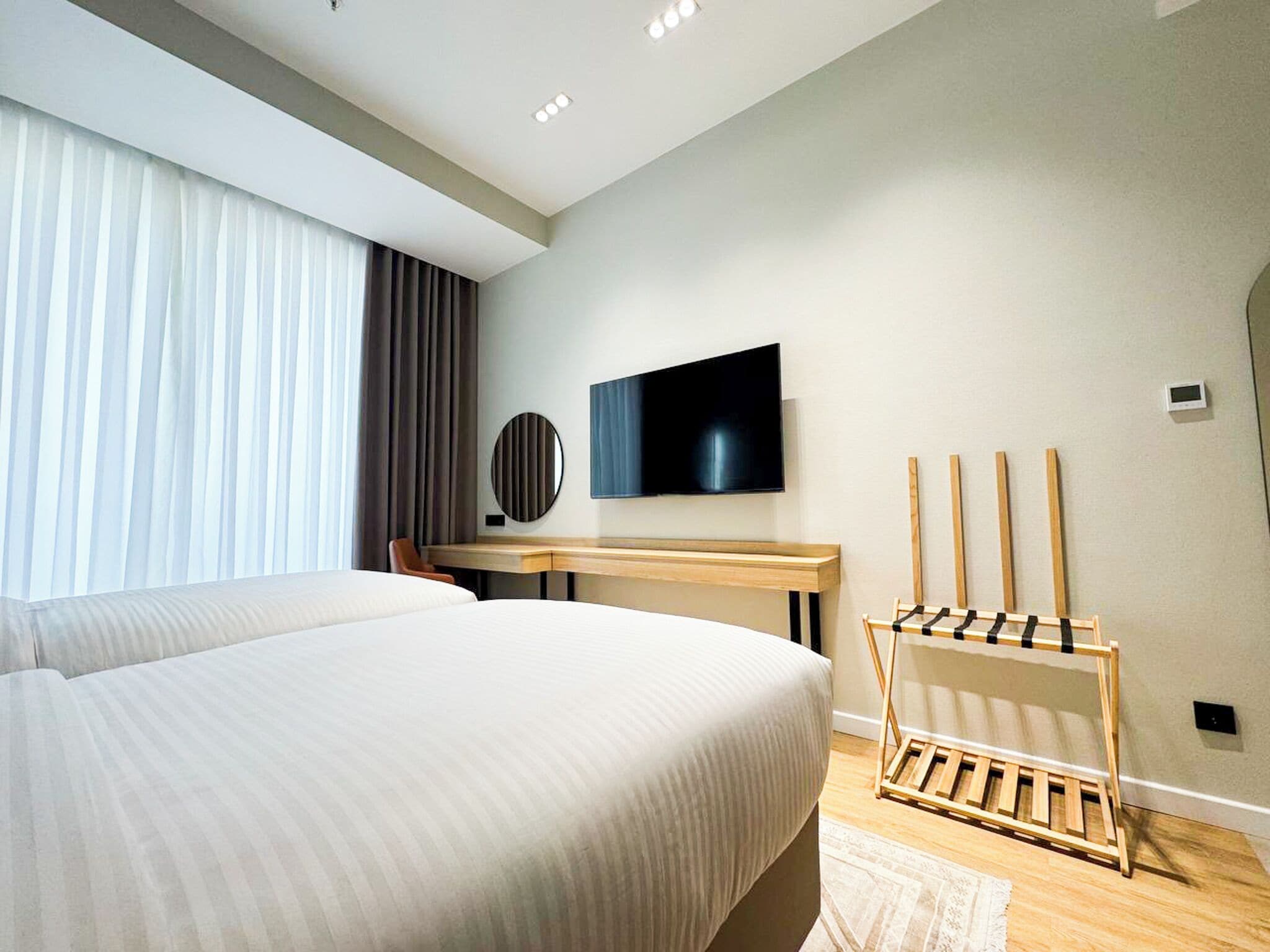 A modern hotel room with a large bed, a desk, a TV, and a shoe rack.
