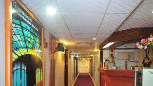 A hotel corridor with a red carpet, a reception desk, and a wall with a colorful stained glass window. - Nice Hotel (Kaohsiung)
