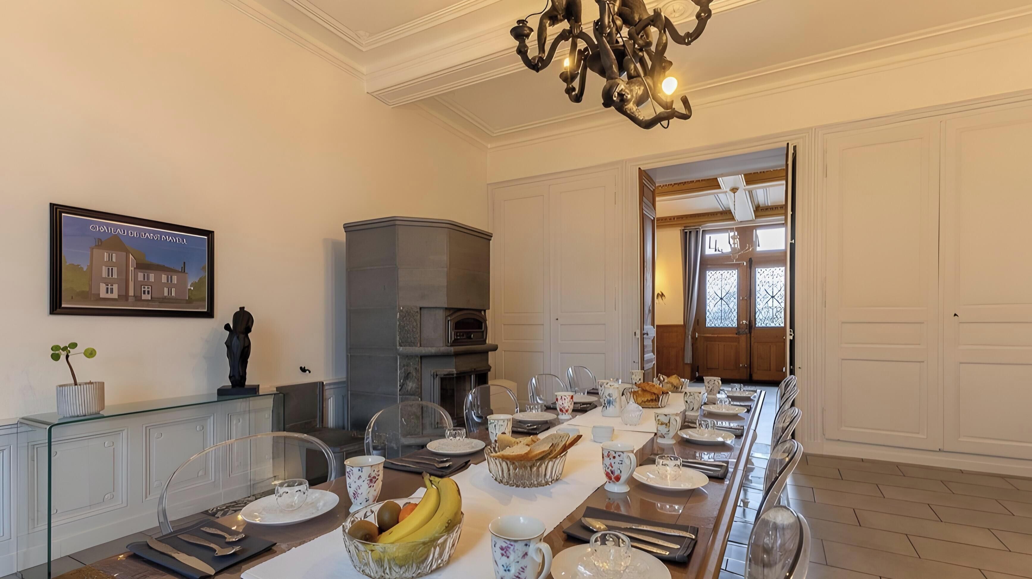 A dining room with a long table set for a meal, a fireplace, and a chandelier.