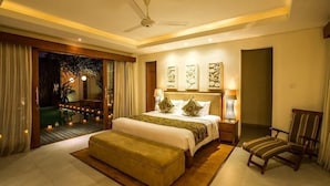 Une chambre d’hôtel moderne dotée d’un grand lit, d’un coin salon avec un fauteuil, d’un ventilateur de plafond et d’œuvres d’art accrochées aux murs.