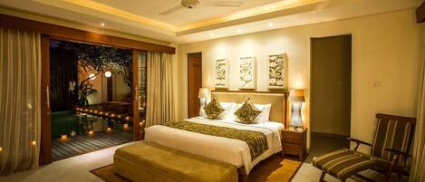 A modern hotel room with a large bed, a sitting area with a chair, a ceiling fan, and artwork on the walls.