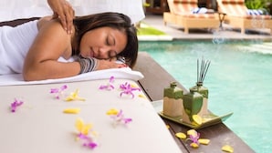 Un espace de détente avec un lit de massage, des fleurs et des bâtonnets d’encens, le tout situé près d’une piscine.