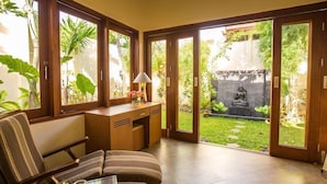 Une pièce comprenant un bureau, une chaise et donnant sur un jardin agrémenté d’une statue.