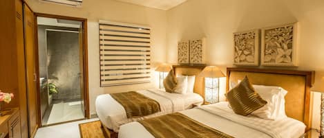 A hotel room with two beds, a wooden headboard, a large window with blinds, and a wall-mounted air conditioner.
