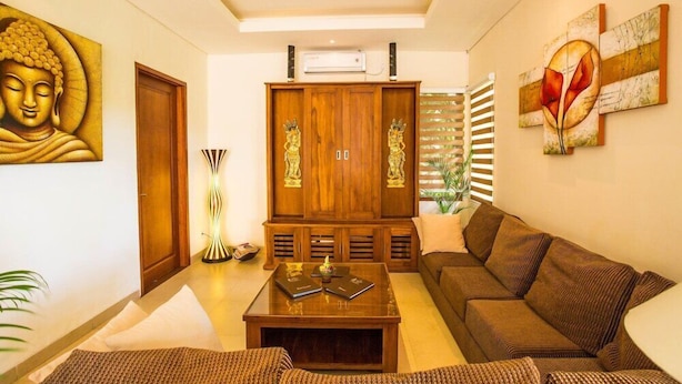 Un salon avec un canapé marron, un meuble en bois et un tableau représentant un Bouddha accroché au mur.