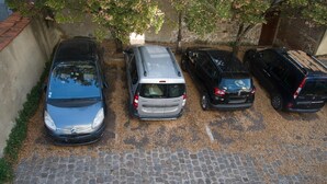 Un espace de stationnement où sont garées cinq voitures, ainsi qu'un chemin pavé.