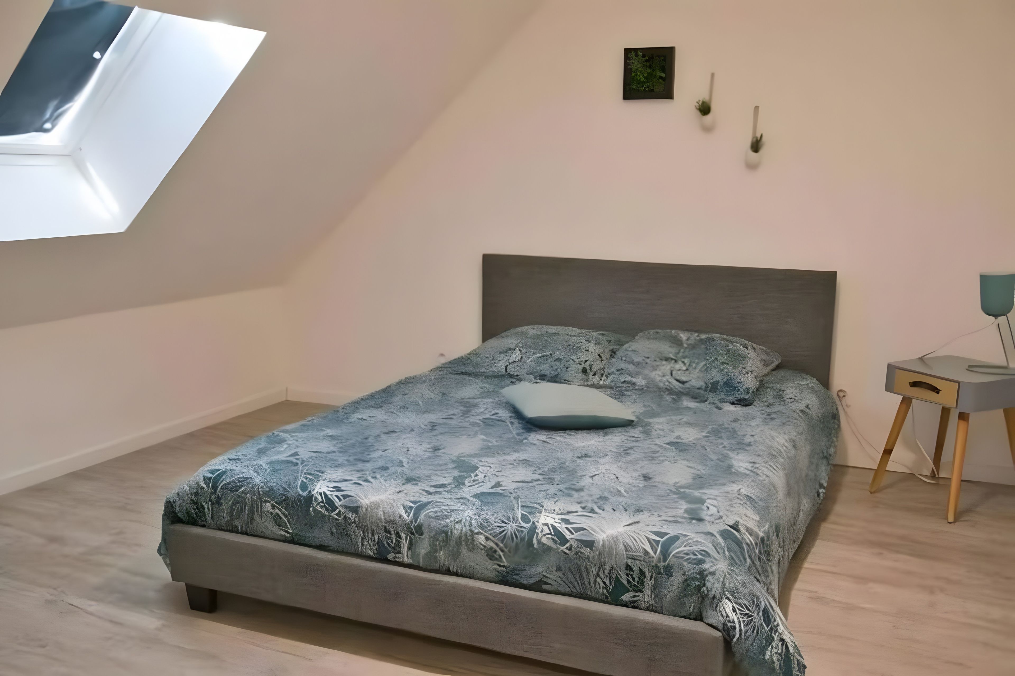 Un dormitori amb un llit, una tauleta de nit, una làmpada de paret i una petita planta.