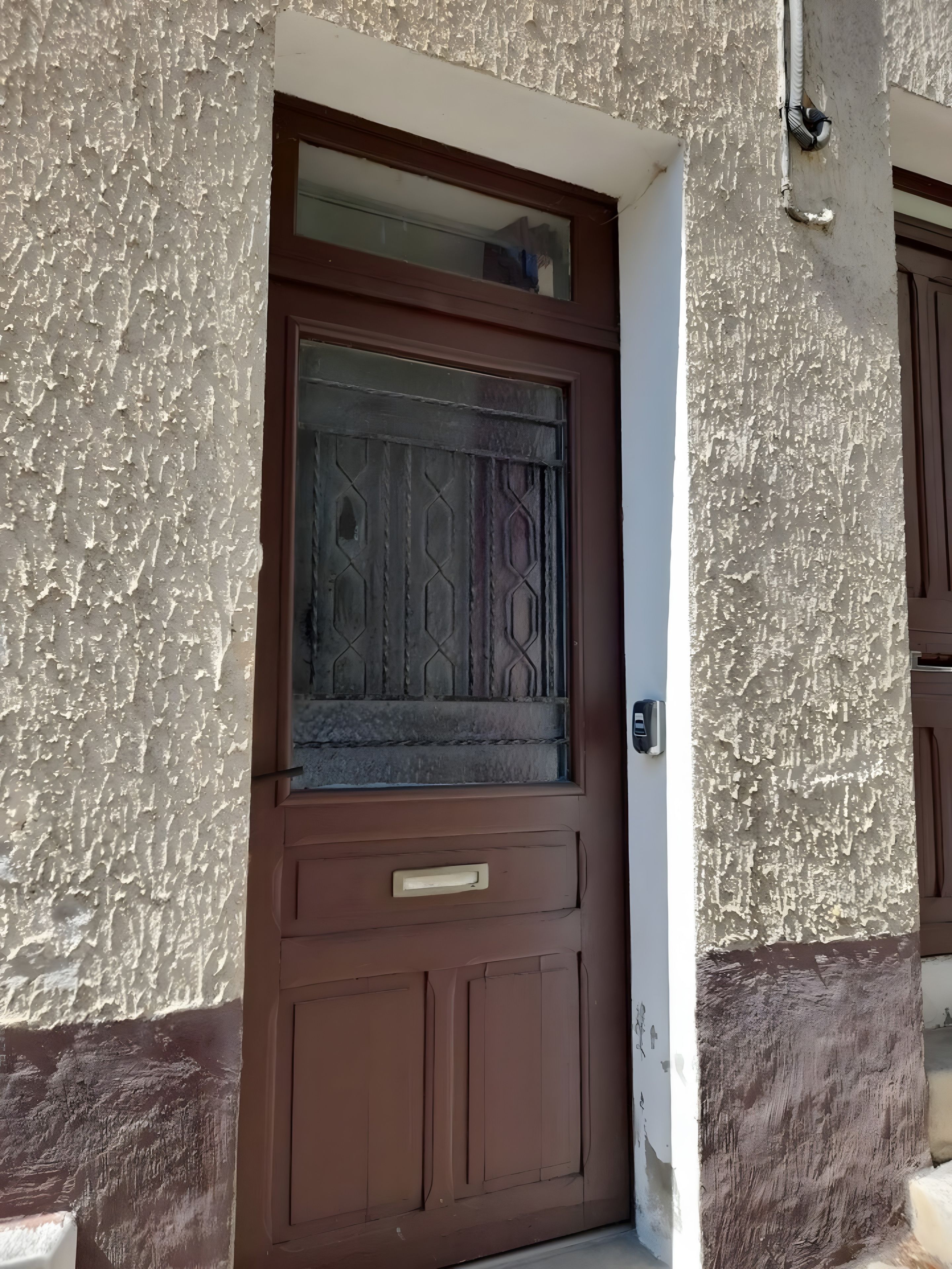 A brown door with a textured wall and a small window above it.