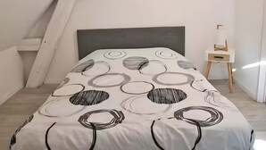 Une chambre avec un plafond en pente, un lit recouvert d’une couvre-lit à motifs circulaires, une table de chevet et des décorations circulaires fixées au mur.