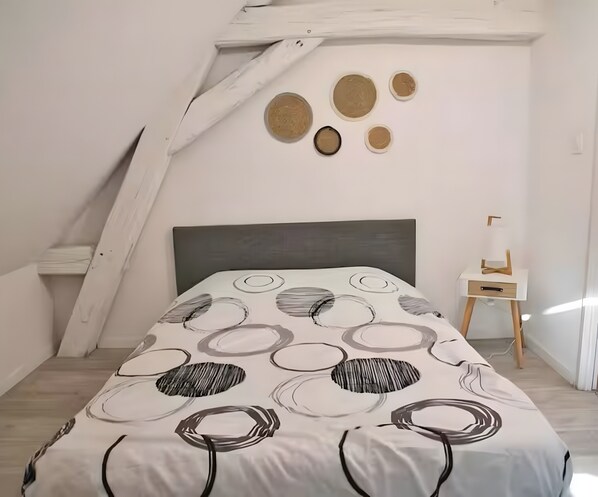 A bedroom with a sloped ceiling, a bed with a circular-patterned bedspread, a bedside table, and wall-mounted circular decorations.