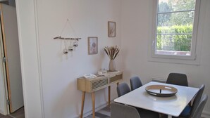 A dining area with a table, chairs, a vase with dried plants, and a window with a view of greenery.