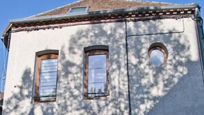 A building with three windows, a door, and a small circular window on the upper floor.