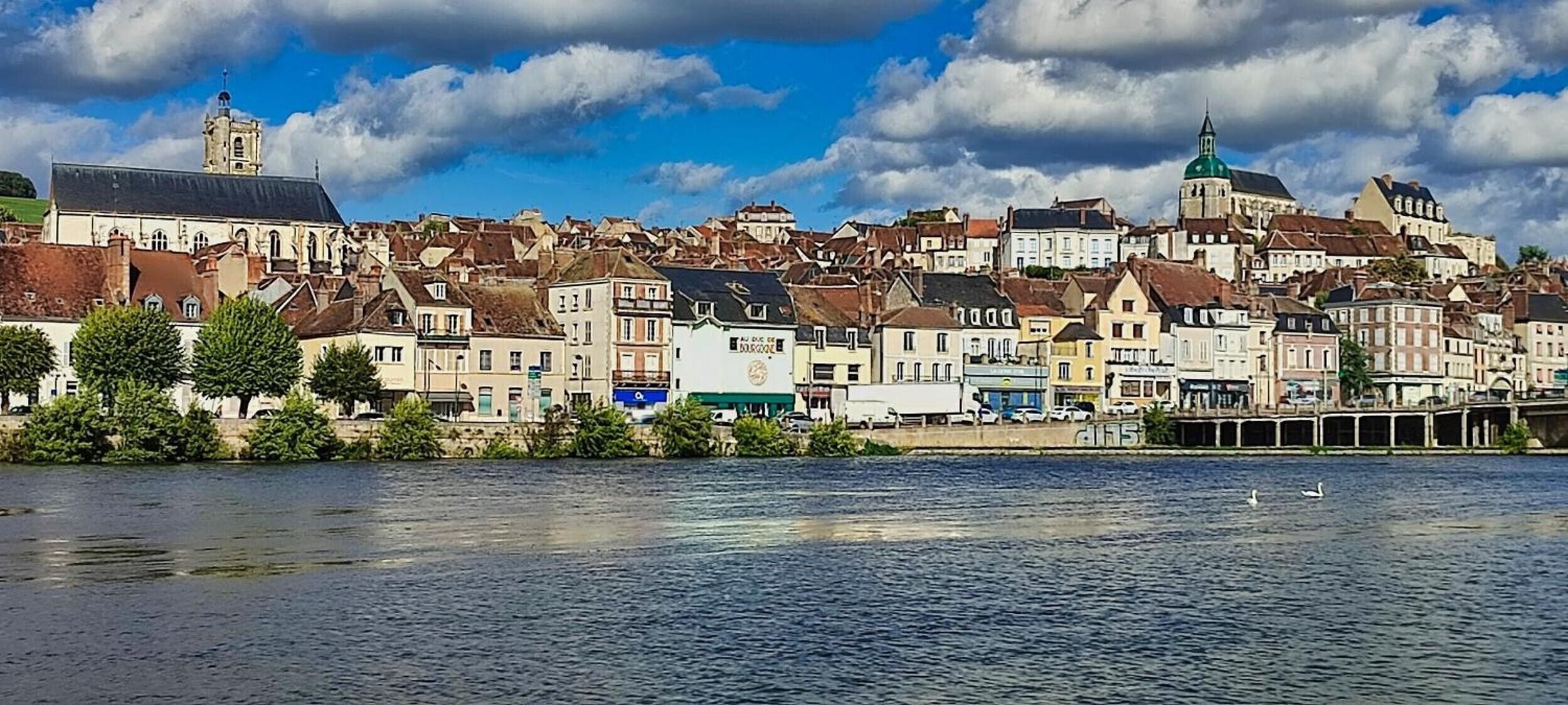 Een pittoresk stadje aan de rivier met historische gebouwen, een opvallende kerk en een brug.