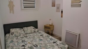 A bedroom with a bed, a bedside table, a wall-mounted TV, and a window with blinds.