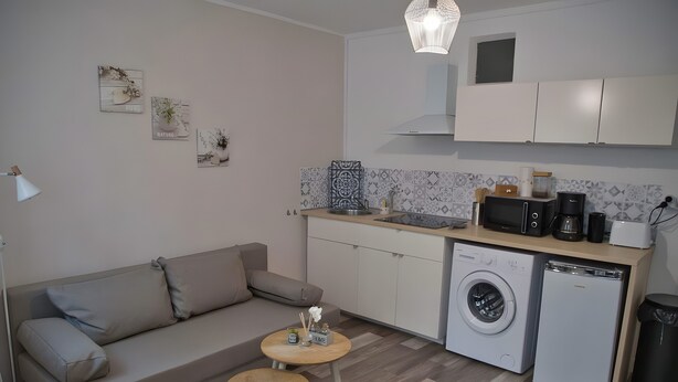 A compact living space with a sofa, a small round table, a washing machine, a microwave, and a coffee maker.