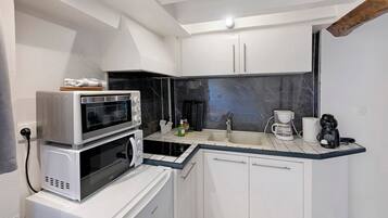 Cocina compacta con gabinetes blancos, microondas integrado, cafetera y un lavamanos.