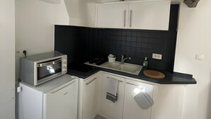 Cocina compacta con microondas, estufa, pileta y alacenas blancas.