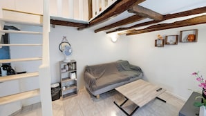 Une pièce confortable avec un lit en mezzanine, un canapé, une petite table et une étagère où sont rangés divers objets.