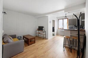 Un espacio habitable moderno con sofá, una mesita, televisor y una cocina con taburetes.