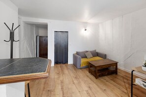 Ein Zimmer mit Holzboden, einem grauen Sofa mit gelbener Decke, einem Holztisch und einem Garderobenschrank.