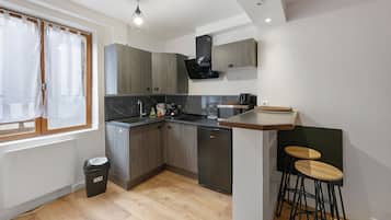 A compact kitchen with a built-in dishwasher, a coffee machine, and a small dining area with stools.