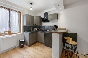 Cocina compacta con lavavajillas integrado, cafetera y un pequeño comedor con taburetes.