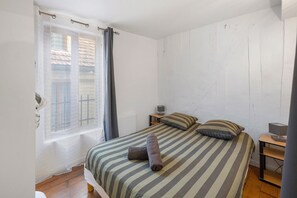 Ein Schlafzimmer mit einem Bett, zwei Kissen, einem Nachttisch mit Lampe und einem Fenster mit Vorhängen.