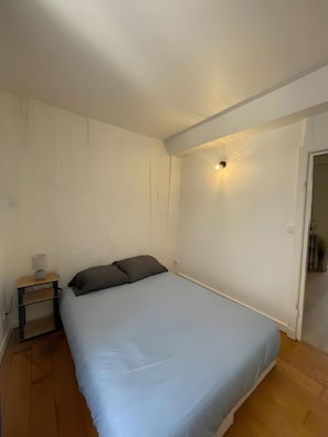 A bedroom with a bed, a nightstand with a lamp, and a wall-mounted light fixture. - Apartment 'Cosy Hypercentre Joigny' with Wi-Fi (Joigny)