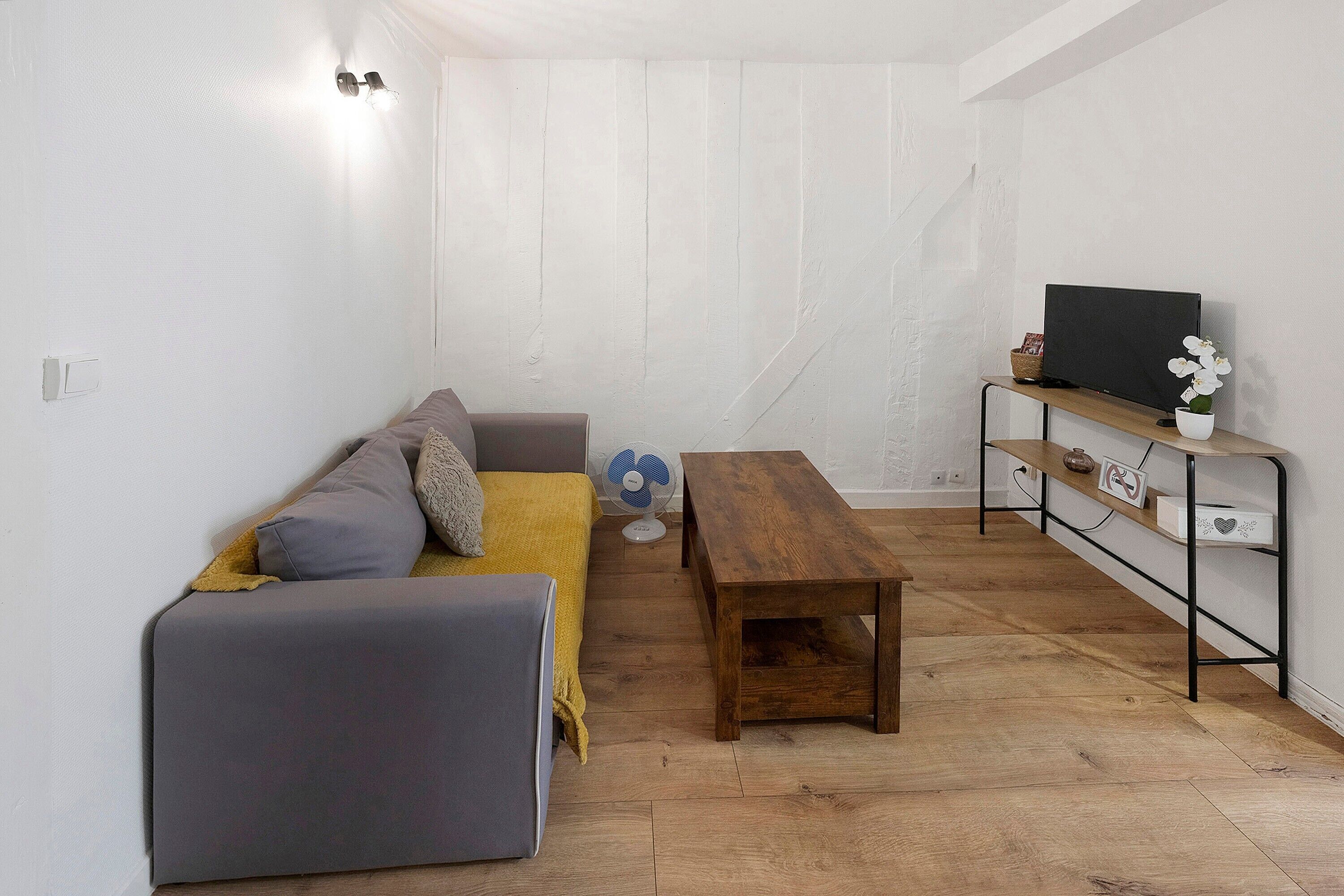 Une petite pièce agréable, avec un canapé gris, une table en bois et un téléviseur posé sur une étagère.