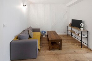 Una habitación pequeña y acogedora con un sofá gris, una mesa de madera y un televisor en un estante.