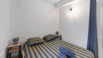 Ein Einzelbett mit gestreifter Bettwäsche, ein Nachttisch mit Lampe und ein Vorhang am Fenster.