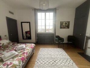 A bedroom with a bed, a chair, a radiator, a window, and a painting on the wall.