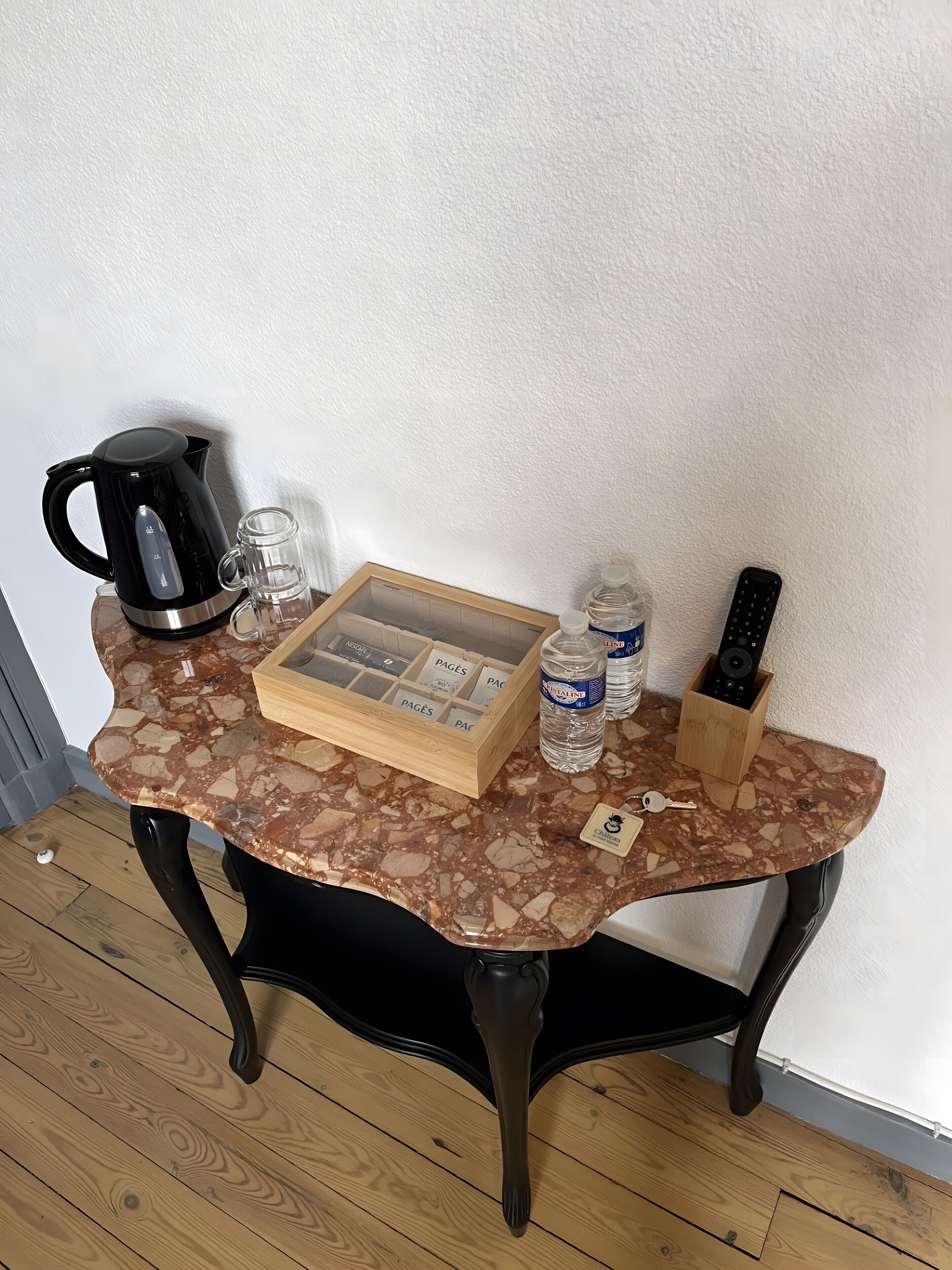 Une petite table sur laquelle se trouvent une machine à café, un verre, une boîte de mouchoirs, une bouteille d’eau et une télécommande.