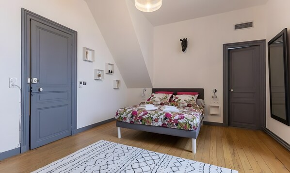 A bedroom with a bed, two doors, a ceiling light, a wall-mounted decoration, and a wooden floor.