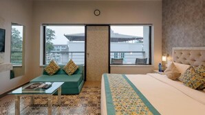 A hotel room with a bed, a sofa, a small table, and a balcony with a view of buildings. - La Sunila Suites (Arpora)