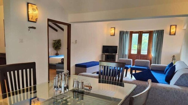 A modern living room with a glass dining table, grey sofas, and a TV. - La Sunila Suites (Arpora)