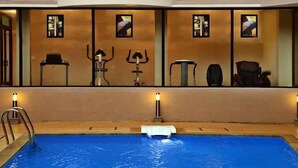 A swimming pool with a diving board, surrounded by a wall with framed pictures and a chair. - La Sunila Suites (Arpora)